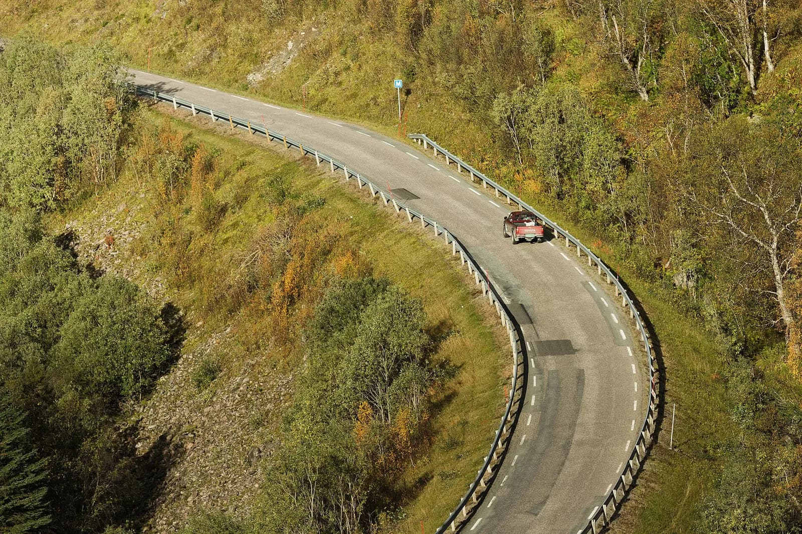 une voiture serpente sur une route de montagne bordée de bouleaux dans le nord de la Norvège